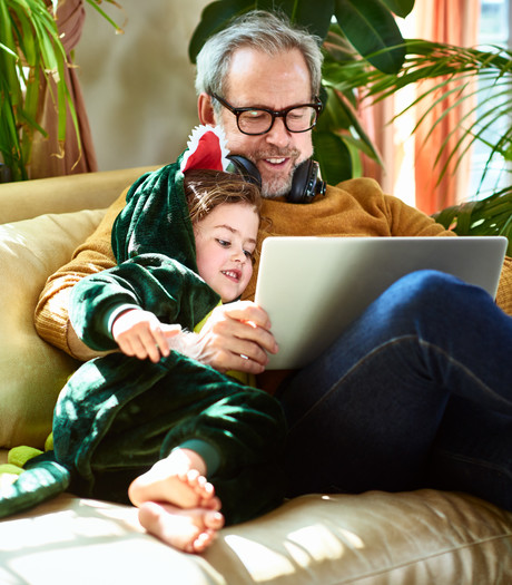 An older male sitting with a young child, smiling at a laptop 