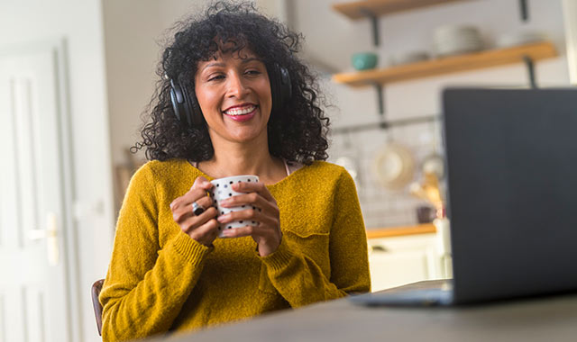 Image of young lady eating breakfast whilst watching a webinar on her laptop computer.